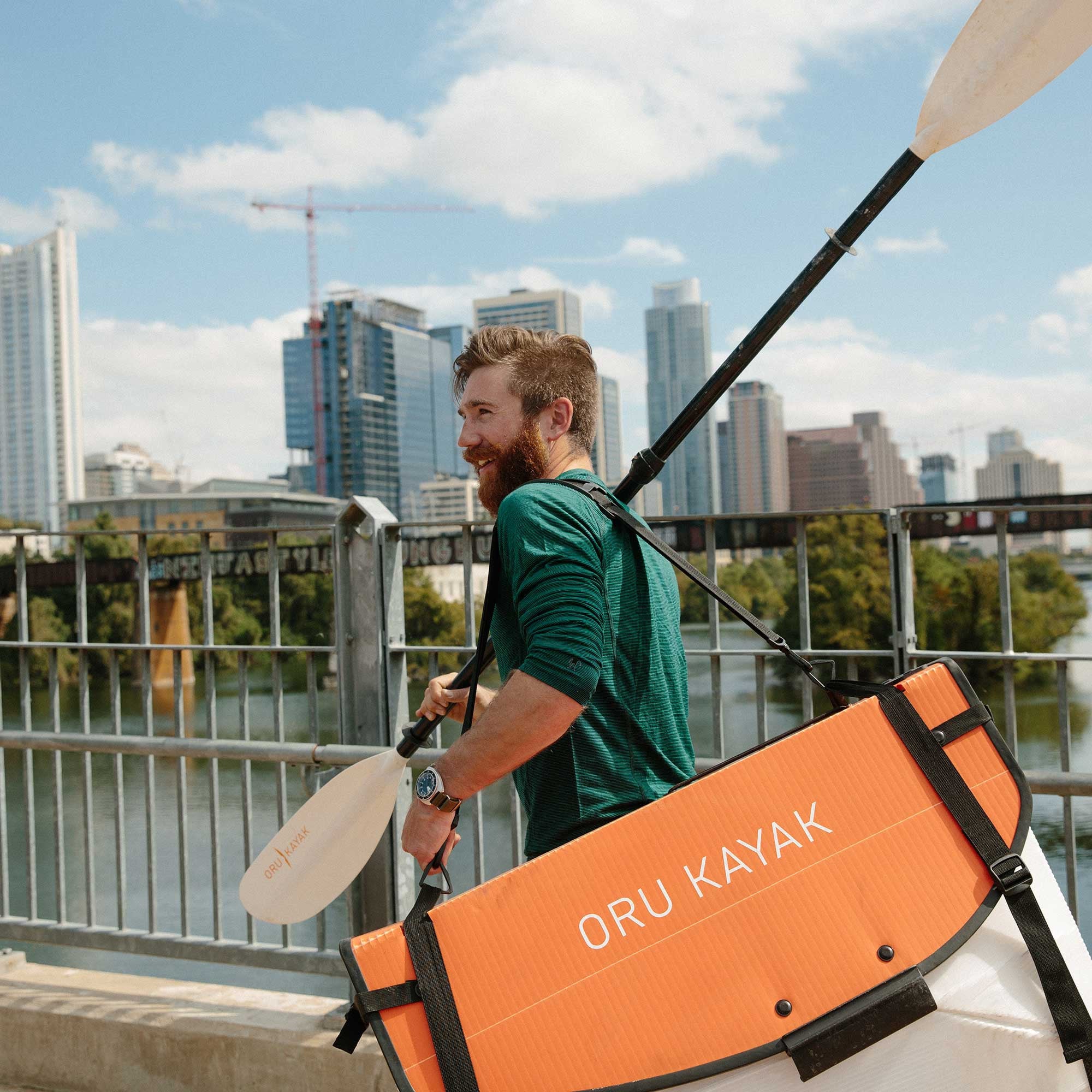 Man carrying bay st folded and paddle across the bridge 
